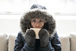 woman-wearing-parka-and-sipping-from-mug-on-couch